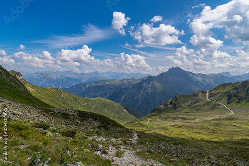 panoramic view over steep Swiss mountains, border with stony rocky mountain with alpine meadows and gravel fields, hikers path way through pasture and boulders up to the summit, holiday destination