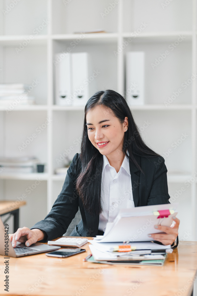 professional woman is working at desk, focused on her laptop while organizing documents and notes. workspace is tidy yet busy, reflecting productive atmosphere. professional woman is working at desk, focused on her laptop while organizing documents and notes. workspace is tidy yet busy, reflecting productive atmosphere.