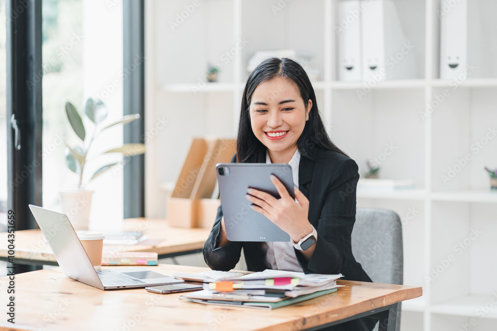 professional woman is smiling while using tablet in modern office setting, surrounded by papers and laptop. Her positive demeanor reflects productivity and engagement. professional woman is smiling while using tablet in modern office setting, surrounded by papers and laptop. Her positive demeanor reflects productivity and engagement.