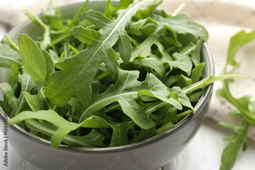 Fresh green arugula leaves in bowl on white table, closeup Fresh green arugula leaves in bowl on white table, closeup