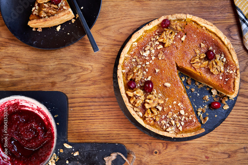 Top view of pumpkin pie with pecans and cranberries lying on a black dish on a black wooden tray photo