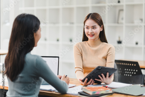Wallpaper Mural Engaged conversation between two women in modern office setting, one holding tablet and other taking notes. atmosphere is collaborative and professional. Torontodigital.ca