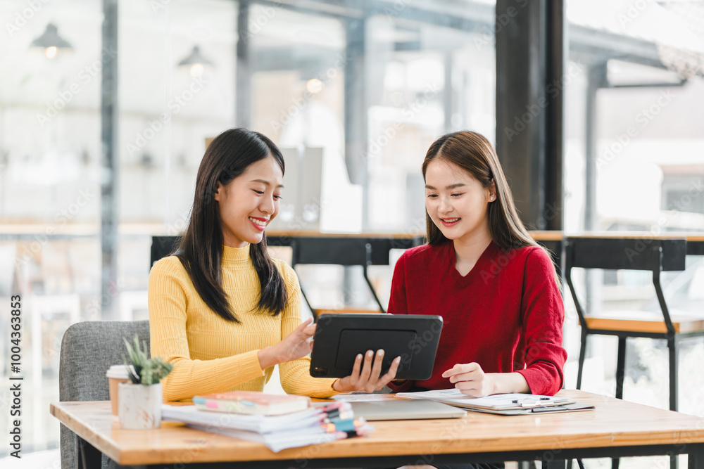 Two women are engaged in collaborative discussion while using tablet in modern cafe setting. They appear focused and friendly, surrounded by books and stationery, creating productive atmosphere. Two women are engaged in collaborative discussion while using tablet in modern cafe setting. They appear focused and friendly, surrounded by books and stationery, creating productive atmosphere.