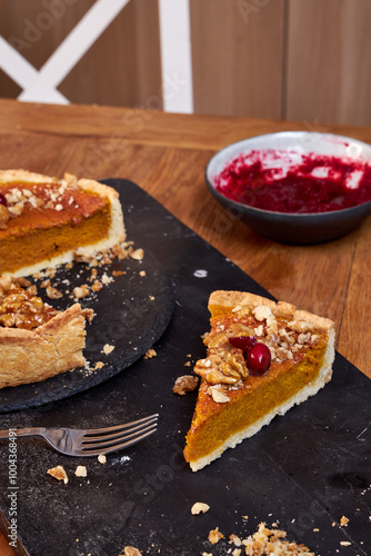 Top view of pumpkin pie with pecans and cranberries lying on a black dish on a black wooden tray