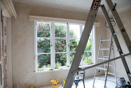 Renovation in progress inside a room with an open window overlooking a garden, featuring a ladder, tools, and unpainted walls, Auckland, New Zealand