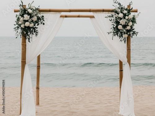 Elegant beach wedding arch adorned with white fabric and flowers on sandy shore, ocean view in the background. photo