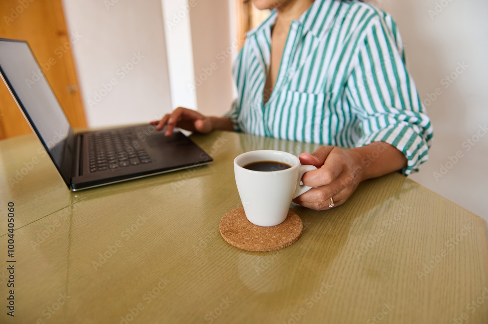 Woman working on a laptop with a coffee cup at home Woman working on a laptop with a coffee cup at home