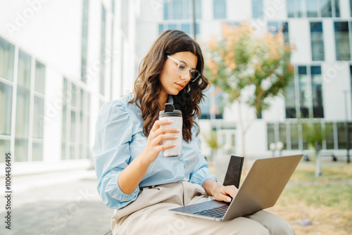 Young businesswoman is working on laptop in front of modern building 