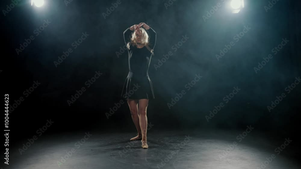 Graceful blonde woman in black dress dancing alone in dark studio, slow motion. Beautiful lady performing contemporary choreography on stage, rehearsing in dance hall, bright soffit and artistic smoke Graceful blonde woman in black dress dancing alone in dark studio, slow motion. Beautiful lady performing contemporary choreography on stage, rehearsing in dance hall, bright soffit and artistic smoke