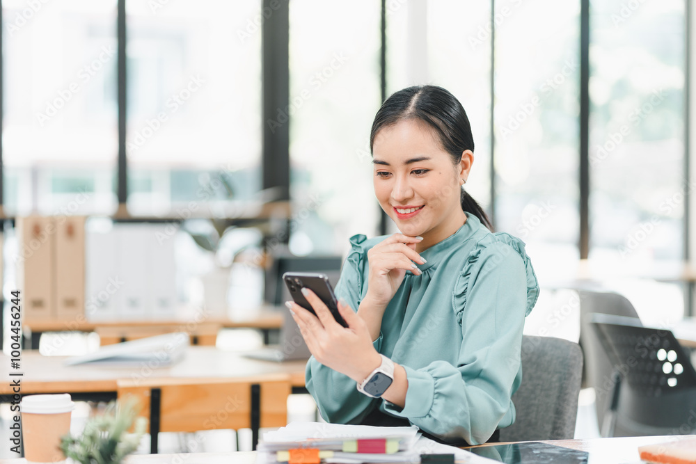 woman is sitting in modern office, smiling while looking at her smartphone. bright and airy environment enhances her cheerful expression, reflecting productive atmosphere. woman is sitting in modern office, smiling while looking at her smartphone. bright and airy environment enhances her cheerful expression, reflecting productive atmosphere.