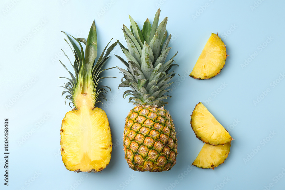 Whole and cut ripe pineapples on light blue background, flat lay