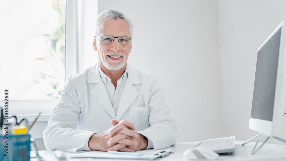 Portrait of smiling senior doctor sitting desktop in medical office Portrait of smiling senior doctor sitting desktop in medical office