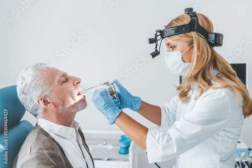 Adult otolaryngologist making endoscopic examination of an oral cavity for senior patient at office photo