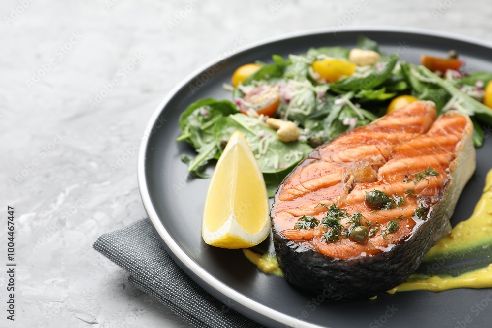 Tasty grilled salmon steak with lemon, sauce and salad on grey textured table, closeup. Space for text Tasty grilled salmon steak with lemon, sauce and salad on grey textured table, closeup. Space for text