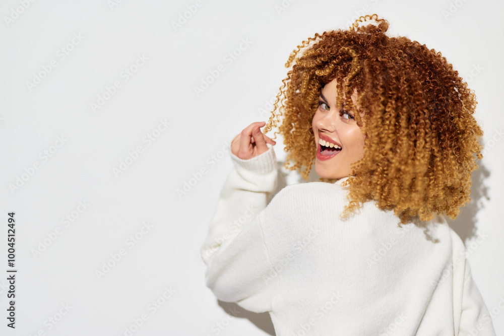 Portrait of a joyful woman with curly hair wearing a cozy white sweater, smiling and looking back over her shoulder against a simple light background Portrait of a joyful woman with curly hair wearing a cozy white sweater, smiling and looking back over her shoulder against a simple light background