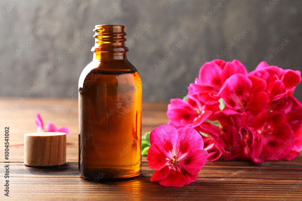 Geranium essential oil in bottle and beautiful flowers on wooden table Geranium essential oil in bottle and beautiful flowers on wooden table