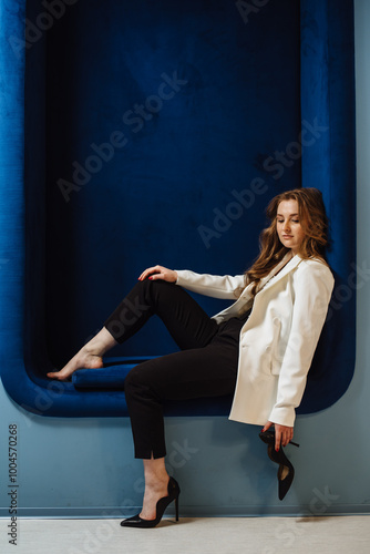 Portrait of a beautiful woman with long curly hair on a blue background. Businesswoman in a white jacket and high heels. Luxurious women. Copy space.