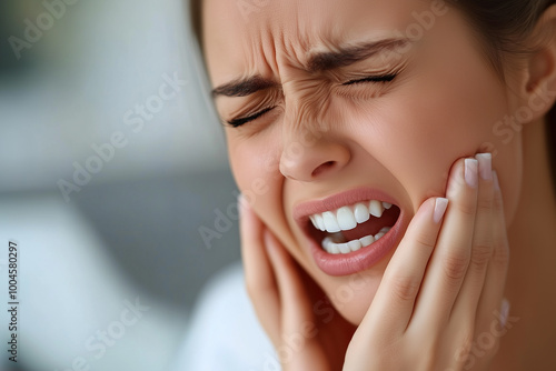 A woman is in pain and is holding her face. She has a toothache and is clenching her teeth