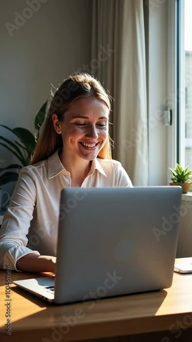 A woman is sitting at a desk with a laptop in front of her. She is smiling and she is enjoying her work