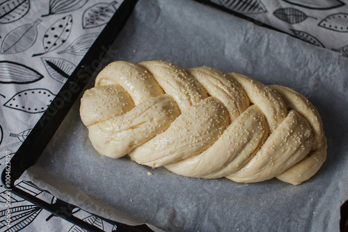 Braided bread with sesame seeds on a baking sheet before cooking photo