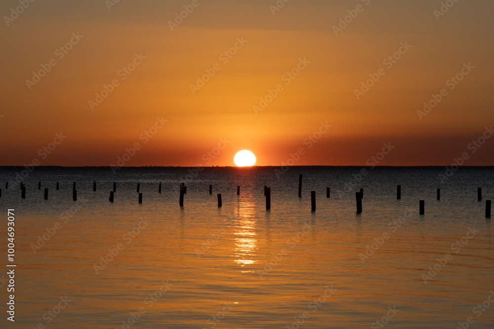 Fototapeta premium Orange sunset with wood pilings on Lake George, part of the St Johns River in Florida