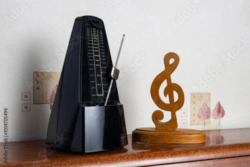 Canvas Print Traditional black metronome next to wooden treble clef on top of an upright pian