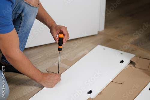 Young man assembling a piece of furniture in his home. With screwdriver and tools in hand to follow the instruction book. Home handyman. He is the owner. New house, new furniture. photo