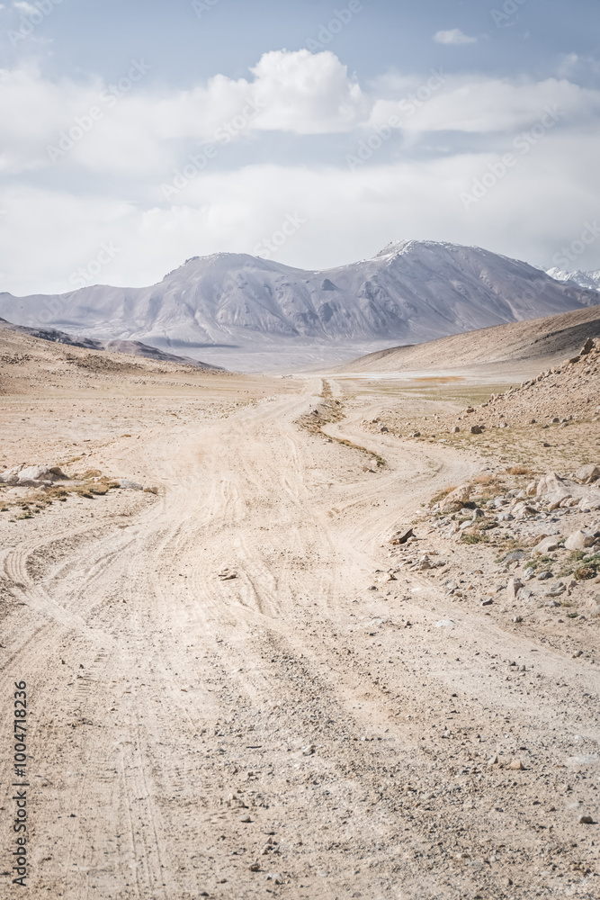 Dusty road of the Pamir Highway winds and twists in the valley of the Tien Shan mountains in Tajikistan in Pamir, landscape in the high desert mountains for background Dusty road of the Pamir Highway winds and twists in the valley of the Tien Shan mountains in Tajikistan in Pamir, landscape in the high desert mountains for background