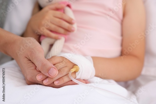 Mother and her little daughter with IV drip on bed in hospital, closeup