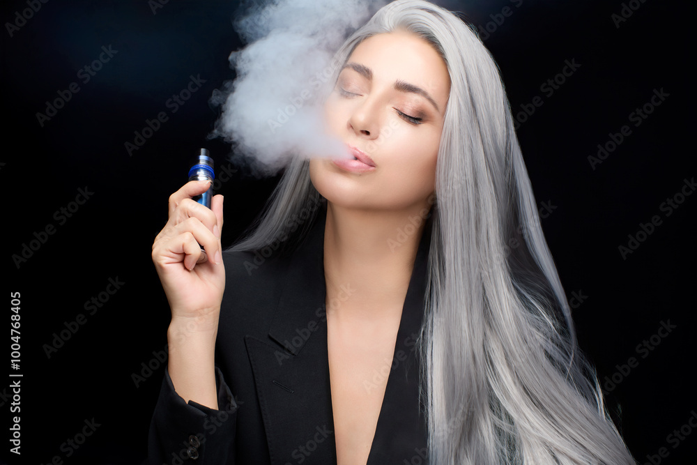 Obraz premium Stylish woman with gray hair vaping on a black background, exhaling cloud of vapor, conveying relaxation and modern lifestyle