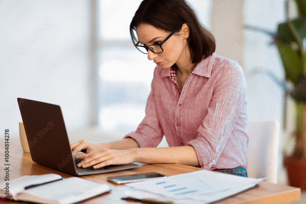 Home Office. Portrait of young woman in eyewear using laptop, working remotely, free space Home Office. Portrait of young woman in eyewear using laptop, working remotely, free space