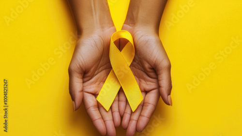 Hands holding a yellow awareness ribbon symbolizing suicide prevention or bone cancer awareness on a bright yellow background. Support for servicemen and prisoners of war and suicide prevention.