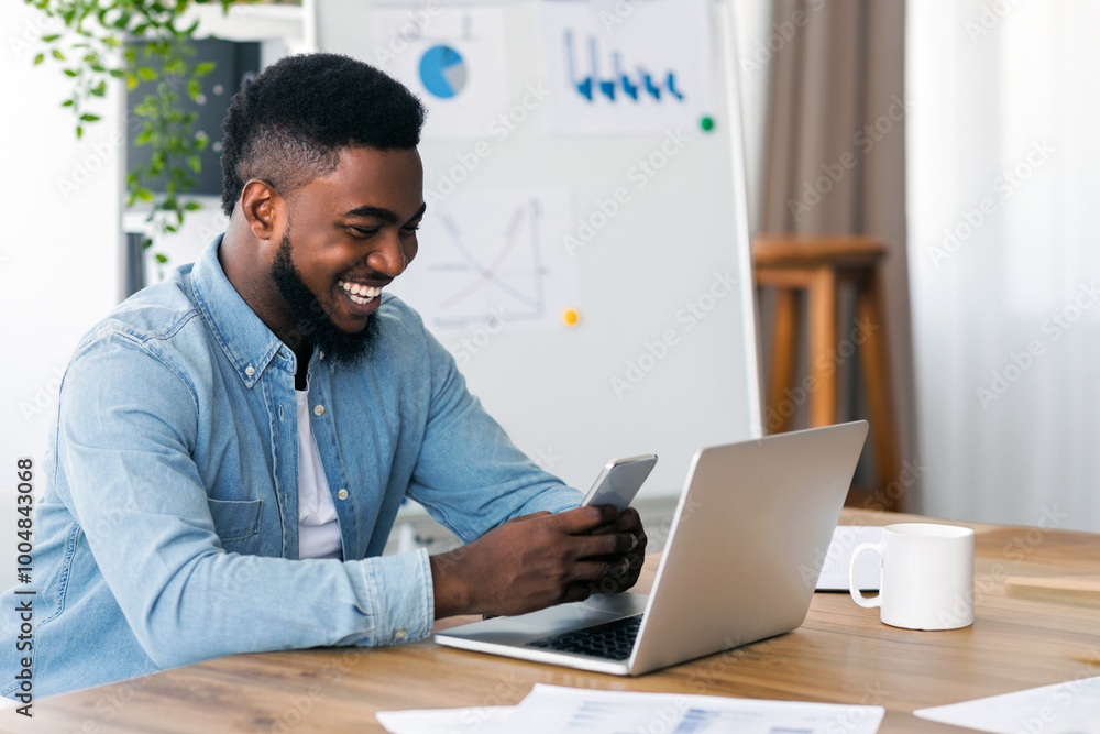 Cheerful african american employee browsing internet on smartphone, having break at work in modern office. Cheerful african american employee browsing internet on smartphone, having break at work in modern office.
