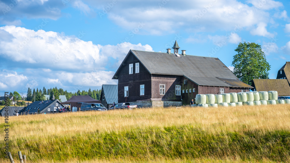 Golden fields surround the rustic homes of Jizerka village, nestled in the scenic Jizera Mountains. A perfect day showcases the peaceful blend of nature and traditional architecture against a bright Golden fields surround the rustic homes of Jizerka village, nestled in the scenic Jizera Mountains. A perfect day showcases the peaceful blend of nature and traditional architecture against a bright