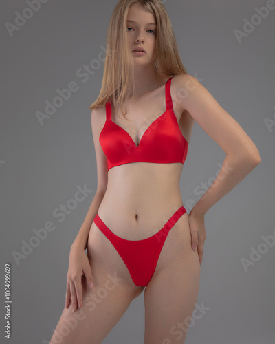 The model stands confidently in a vibrant red lingerie set, highlighting the smooth fabric and elegant design. The neutral background emphasizes her pose and the outfit’s details.