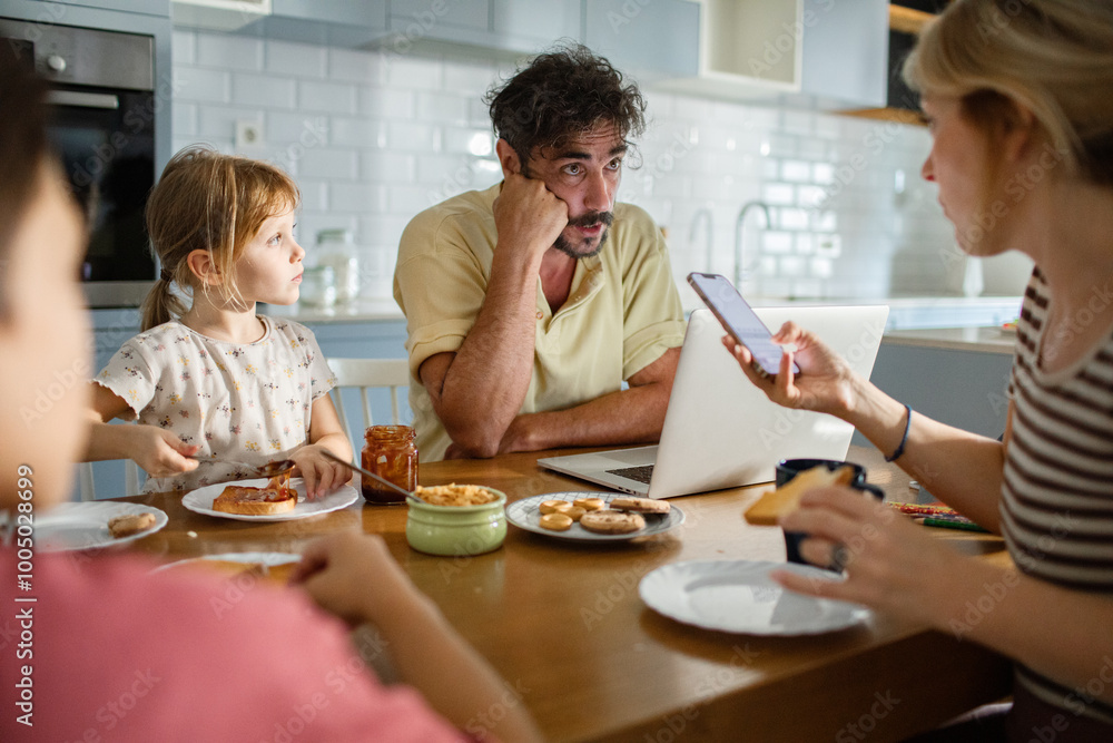 Father working on laptop while family has breakfast in kitchen Father working on laptop while family has breakfast in kitchen
