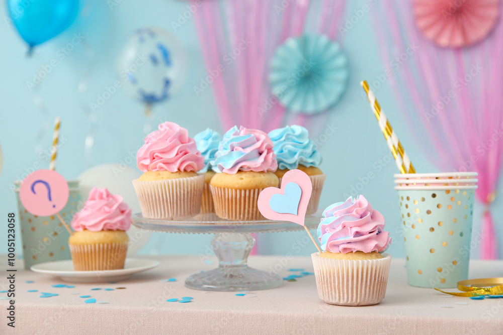 Delicious cupcakes with cups and decorations on table against blue background. Gender reveal party concept Delicious cupcakes with cups and decorations on table against blue background. Gender reveal party concept
