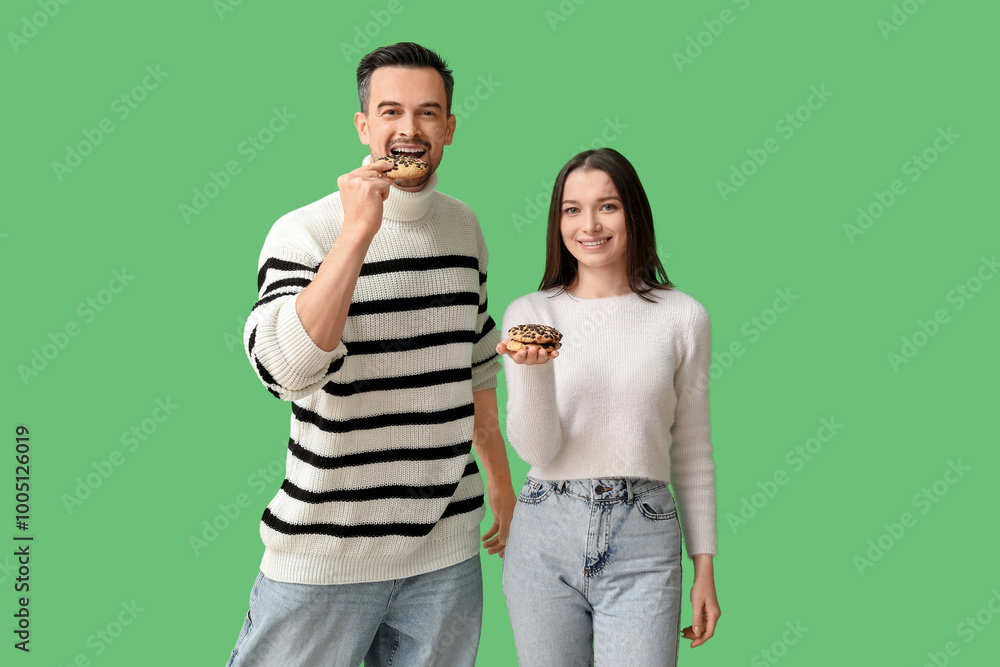 Young couple with tasty cookies on green background Young couple with tasty cookies on green background
