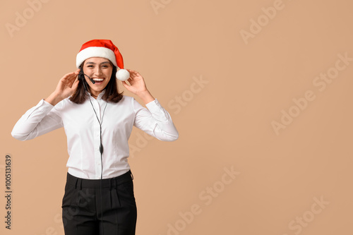 Beautiful female technical support agent in Santa hat on brown background