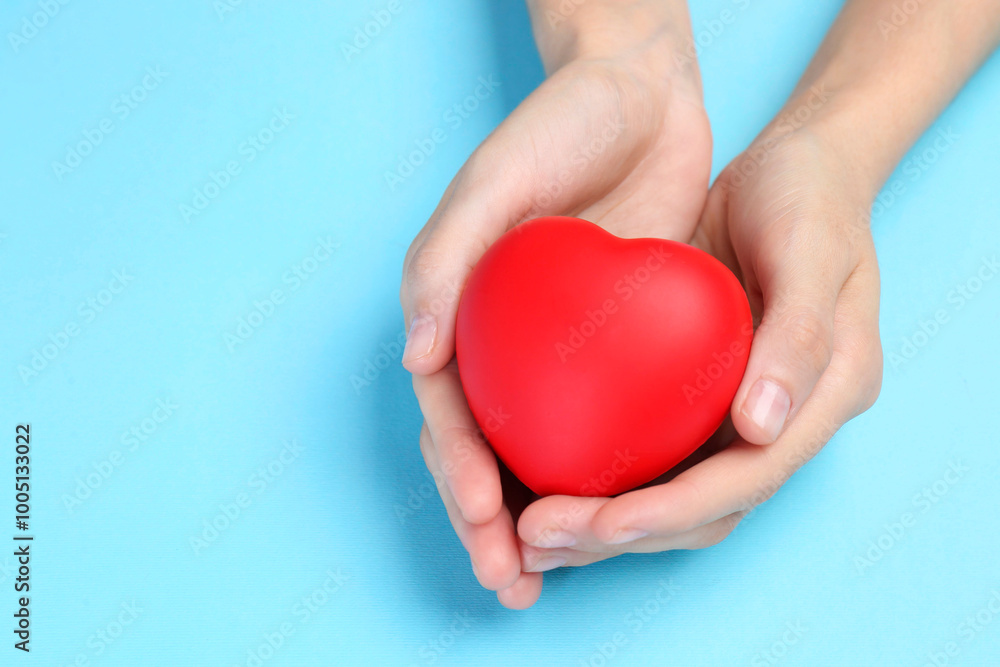 Woman holding red heart on light blue background, closeup. Space for text