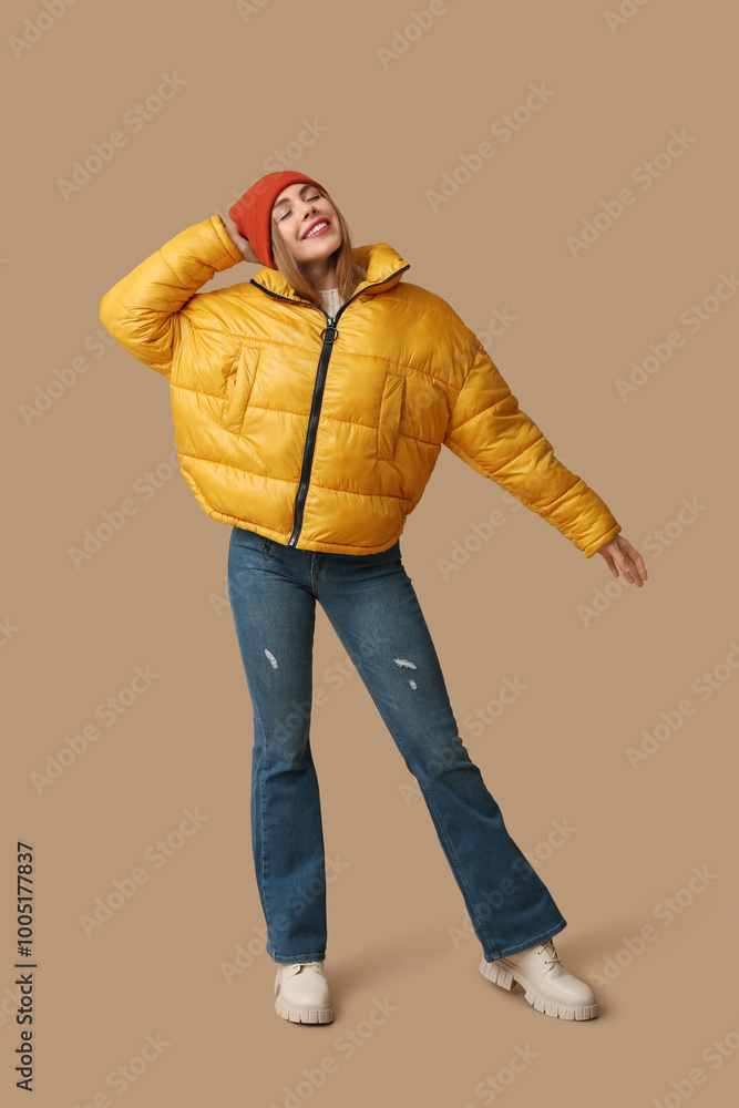 Fototapeta premium Beautiful young happy woman in warm winter clothes on brown background