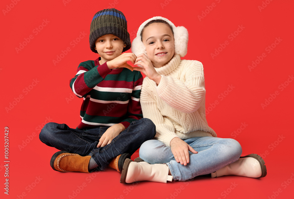Cute little children in warm winter clothes showing heart gesture on red background Cute little children in warm winter clothes showing heart gesture on red background