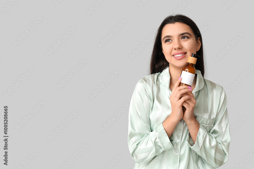 Beautiful young woman with bottle of cosmetic product on grey background Beautiful young woman with bottle of cosmetic product on grey background