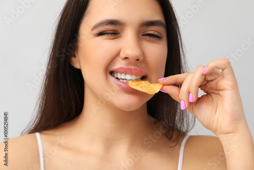 Young woman with beautiful lips eating potato chip on grey background, closeup