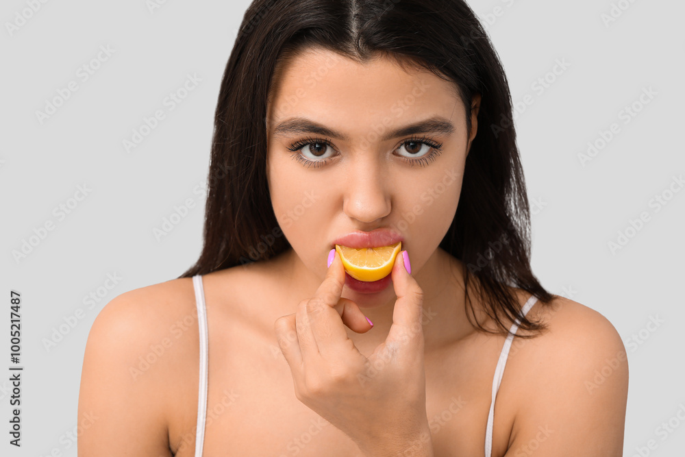 Beautiful young woman eating lemon on grey background, closeup Beautiful young woman eating lemon on grey background, closeup