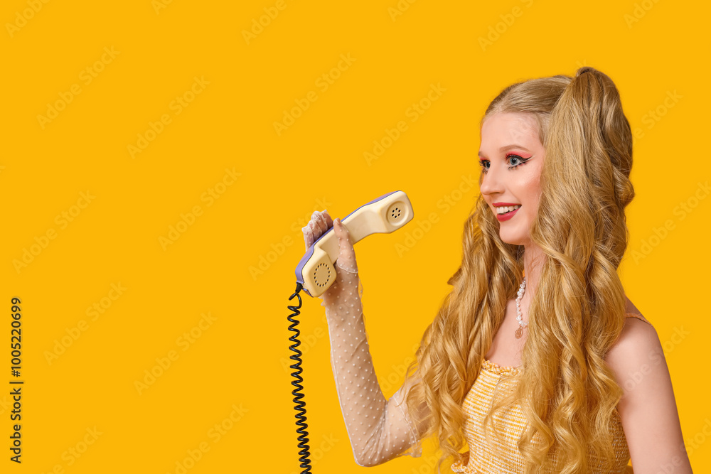 Beautiful young happy woman dressed as doll talking by retro phone on yellow background Beautiful young happy woman dressed as doll talking by retro phone on yellow background