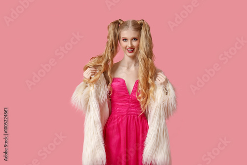 Beautiful young happy woman dressed as doll with stylish fur coat on pink background