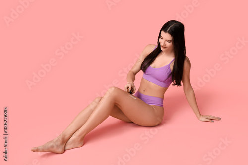 Beautiful young woman with bottle of cream sitting on pink background