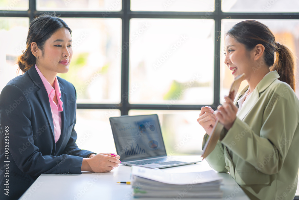 Two successful Asian businesswomen working with financial data graph documents and laptops in business data analysis. Two successful Asian businesswomen working with financial data graph documents and laptops in business data analysis.