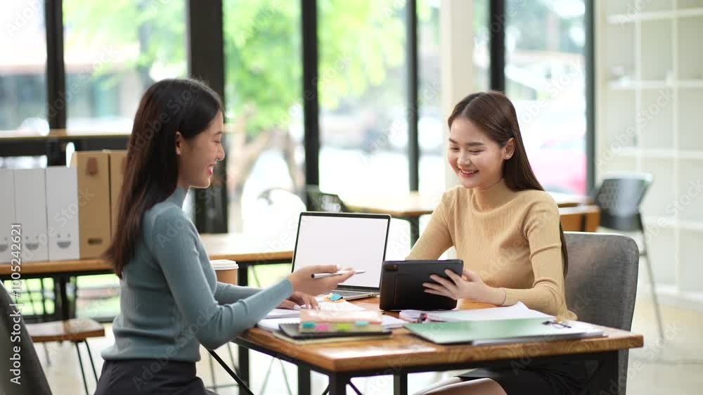Two women engaged in friendly discussion while using tablet and laptop in modern workspace. Their expressions convey collaboration and enthusiasm for their project. Two women engaged in friendly discussion while using tablet and laptop in modern workspace. Their expressions convey collaboration and enthusiasm for their project.